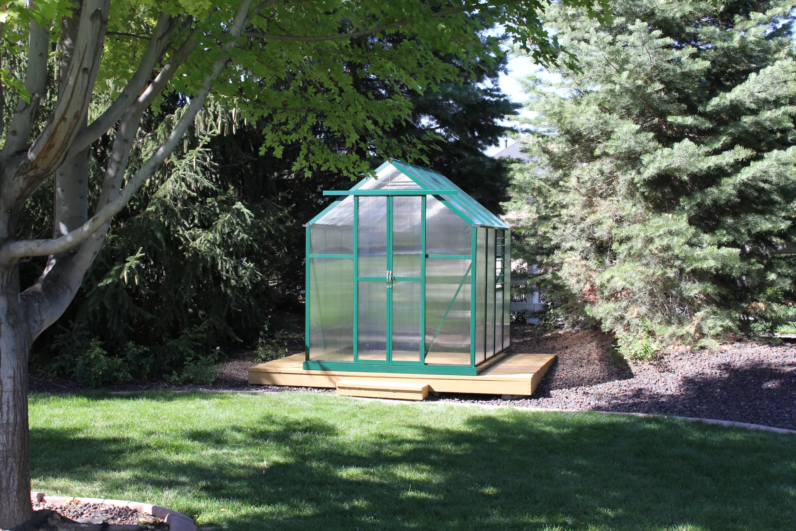 Frontal view of Grandio Element 6x8 greenhouse on a wooden deck, highlighting the spacious entry and peak roof design.