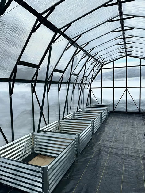 Clean and empty interior of a Grandio greenhouse with raised metal garden beds ready for planting.